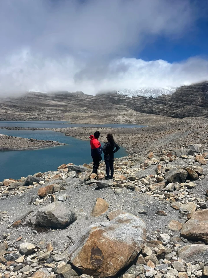 Dos caminantes frente a las lagunas de Laguna Grande de la Sierra, con el glaciar entre nubes al fondo